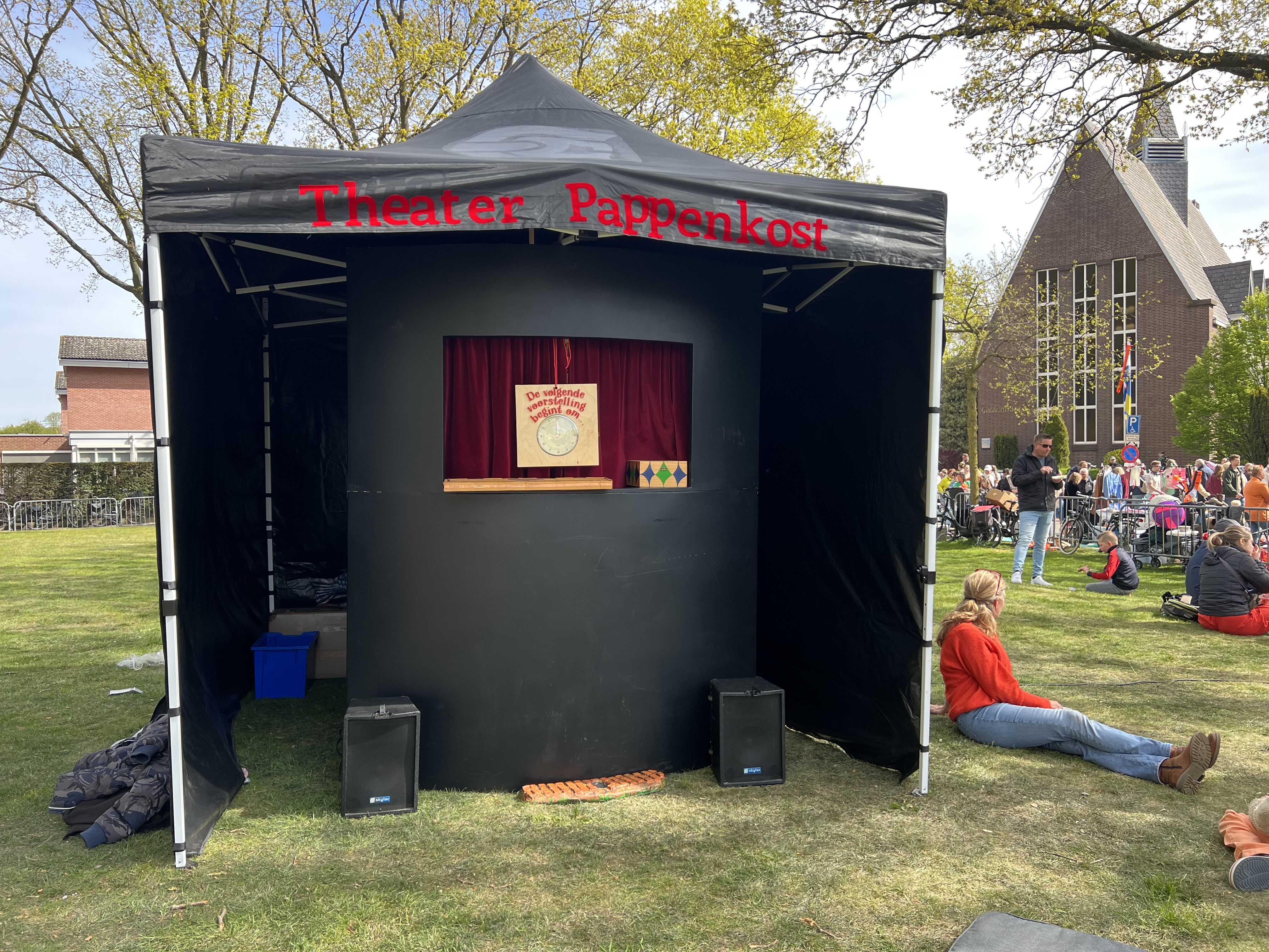 De zwarte theatertent van Theater Pappenkost op een grasveld, met rode letters 'Theater Pappenkost' op de voorkant.